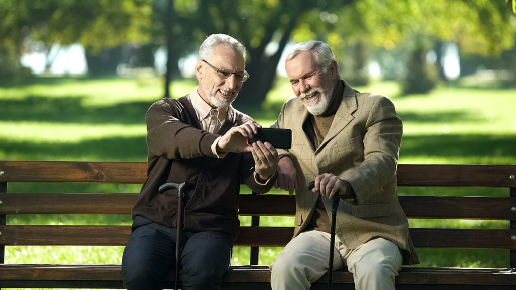 two elderly men sitting on bench looking at phone